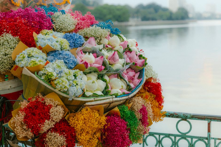 A vibrant arrangement of fresh flowers displayed on a boat near a waterway, featuring large pink and white roses, clusters of blue and white hydrangeas, and various coloured sprigs of baby's breath in