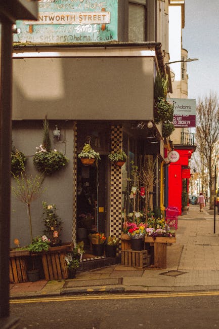 A floral display outside a florist shop features a variety of fresh flowers arranged in pots and baskets, including pink, white, and purple blooms, along with greenery. The flowers are vibrant and app