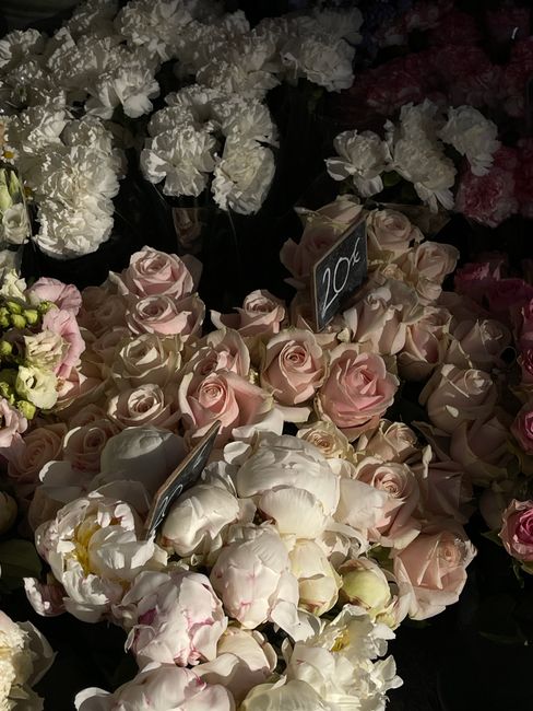 A display of fresh flowers at White City Florist, featuring a variety of pastel pink roses and white peonies arranged in a bouquet with soft, delicate petals. The roses are tightly packed, showcasing